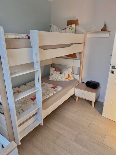 Schlafzimmer II Ein Etagenbett im zweiten Schlafzimmer. Das Bettgestell aus Holz ist weiß. Daneben steht ein Nachttischchen.